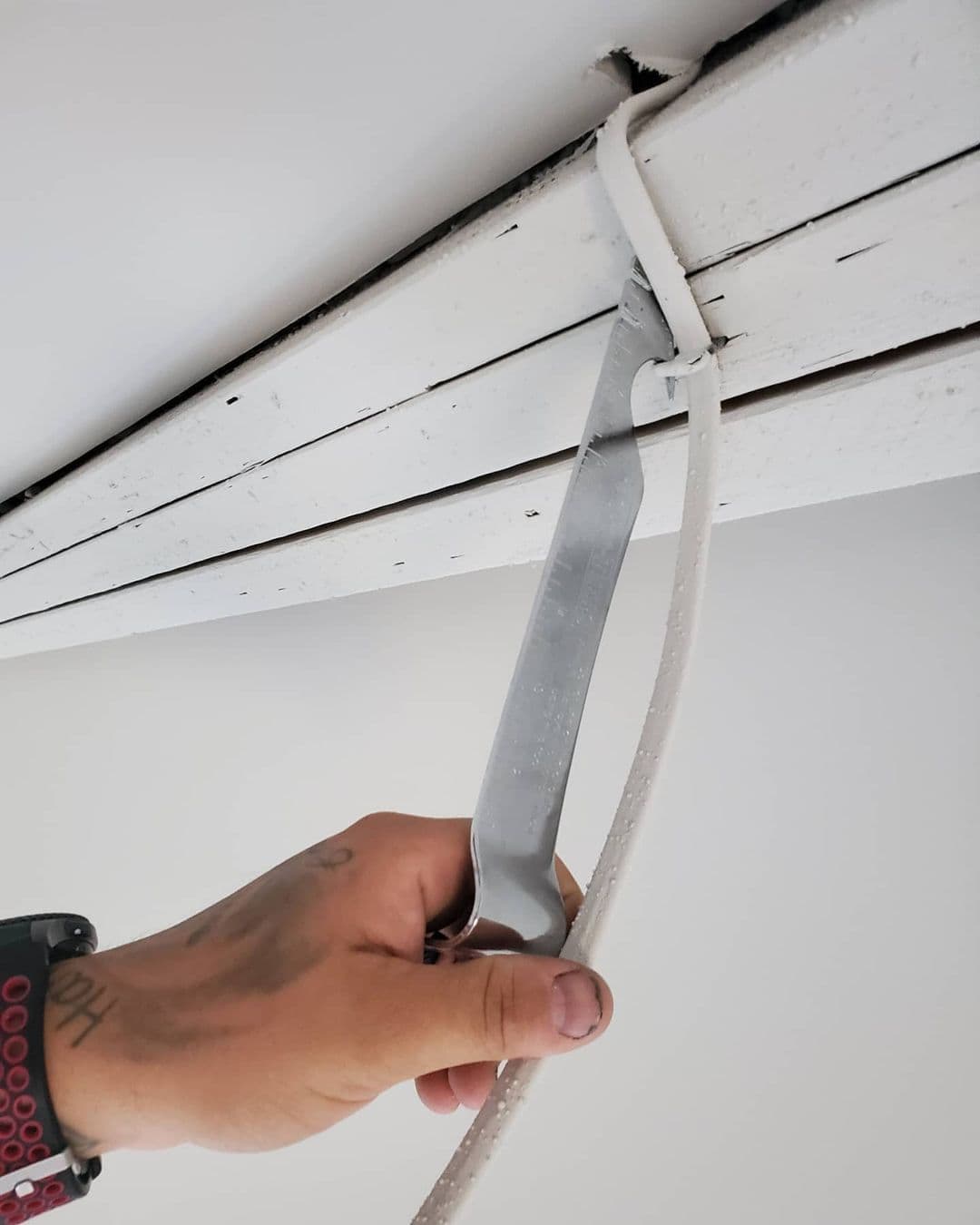 An electrician is using the staple shark to remove a cable staple from some white painted wood.