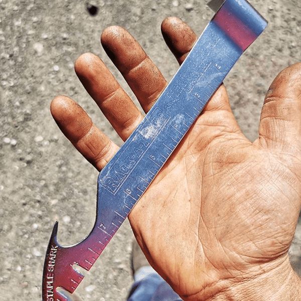 A hand holds the Staple Shark staple remover and pry bar with a Rack-A-Tiers logo etched into the hardened metal.